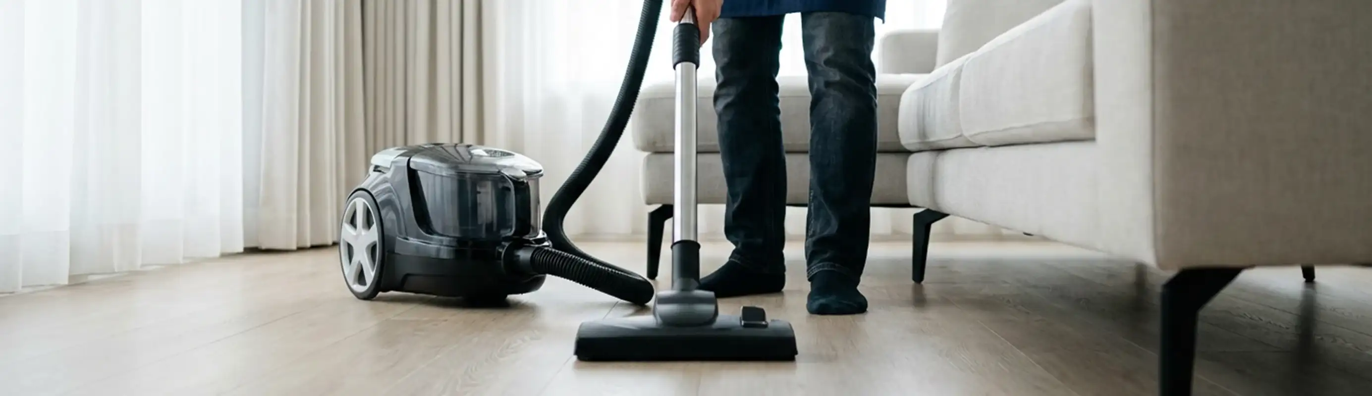 Professional house cleaner vacuuming a living room floor with a canister vacuum cleaner, Kansas City, MO.
