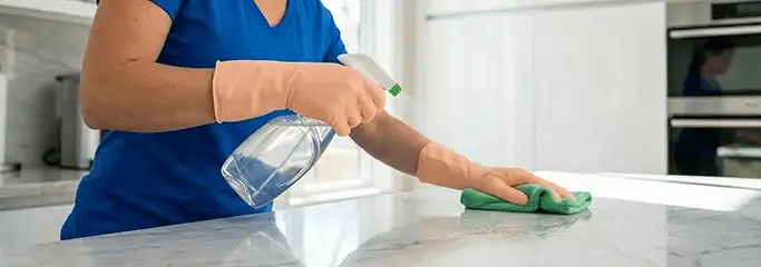 Maid service worker spraying and wiping a kitchen countertop with a microfiber cloth for sanitizing, Kansas City, MO.