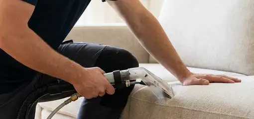 Professional upholstery cleaner deep-cleaning a fabric sofa with a handheld extraction tool, Kansas City, MO.
