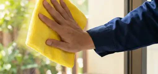 House cleaner wiping a glass window with a yellow microfiber cloth for streak-free cleaning, Kansas City, MO.